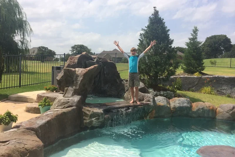 A child stands with his arms out excitedly on a ledge above a pool A child stands with his arms out excitedly on a ledge above a pool