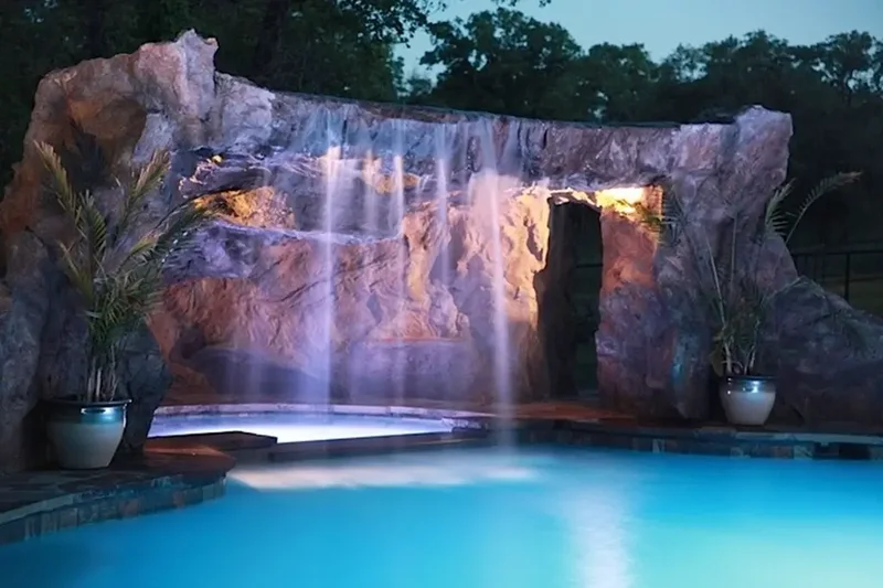 A hardcape water feature over a pool hot tub with a waterfall and built in lighting A hardcape water feature over a pool hot tub with a waterfall and built in lighting